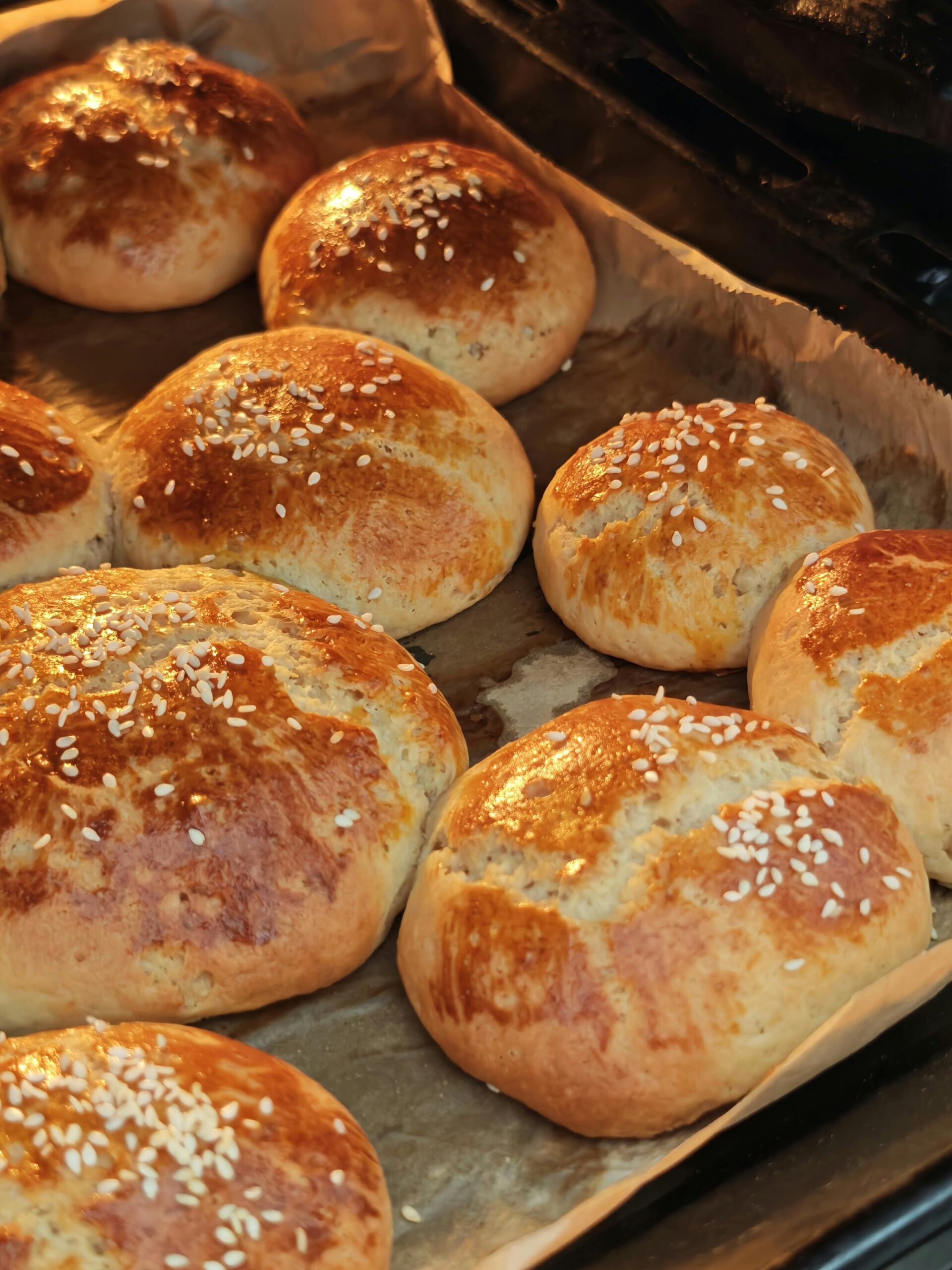 Golden brown homemade bread rolls topped with sesame seeds, fresh out of the oven.
